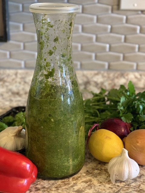 Puerto Rican Sofrito in a glass jar surrounded by ingredients.
