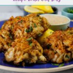 6 Maryland crab cakes arranged on a round blue plate with lemon wedges and remoulade sauce.