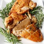 Two pan seared chicken breast, drizzle with brandy pan sauce and surrounded by fresh rosemary, thyme, and garlic.
