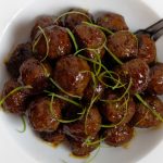 Honey Glazed Garlic And Ginger Meatballs garnished with thinly sliced scallions in a white bowl.