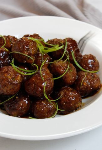Honey Glazed Garlic And Ginger Meatballs garnished with thinly sliced scallions in a white bowl.