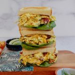 Three stacked curry chicken salad sandwiches on a cutting board.