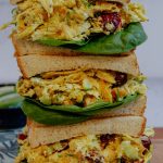 Three stacked curry chicken salad sandwiches on a cutting board.