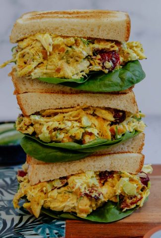 Three stacked curry chicken salad sandwiches on a cutting board.