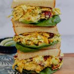 Three stacked curry chicken salad sandwiches on a cutting board.