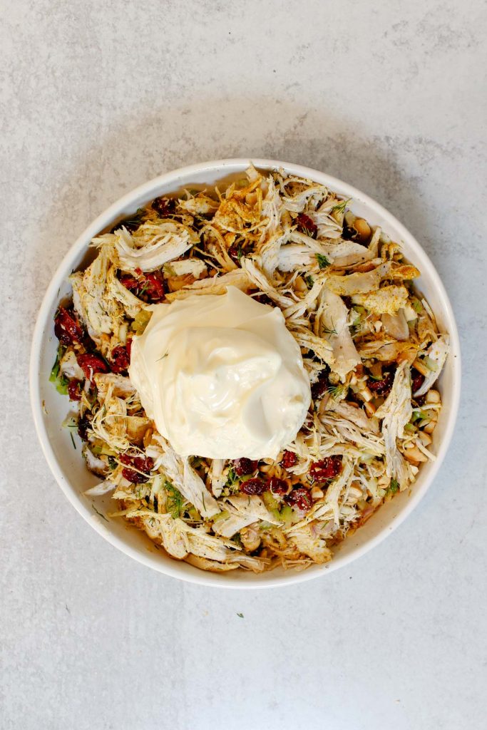 Mayonnaise dolloped on top of a bowl of curry chicken salad ingredients.