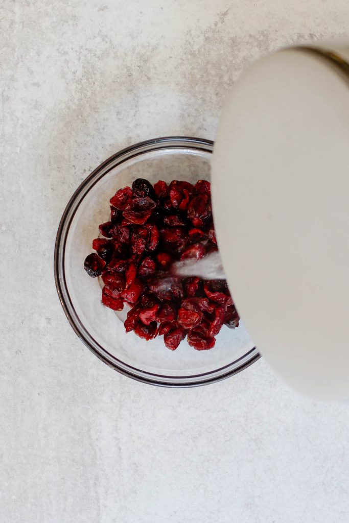 Pouring boiling water over a small bowl of dried cranberries to rehydrate them.