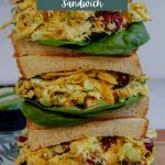 Three stacked curry chicken salad sandwiches on a cutting board.