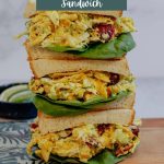 Three stacked curry chicken salad sandwiches on a cutting board.