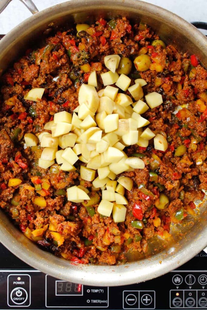 Diced potatoes added to picadillo in a skillet.