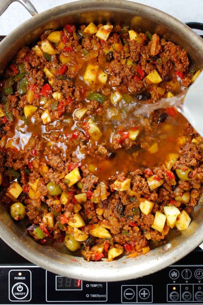 Water added to picadillo in a skillet.