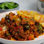 Puerto Rican picadillo plated with white rice and tostones on a pick plate, next to a large skillet filled with picadillo.