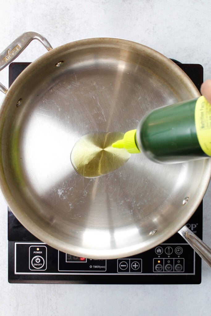 Pouring olive oil into an all-clad stainless steel skillet.