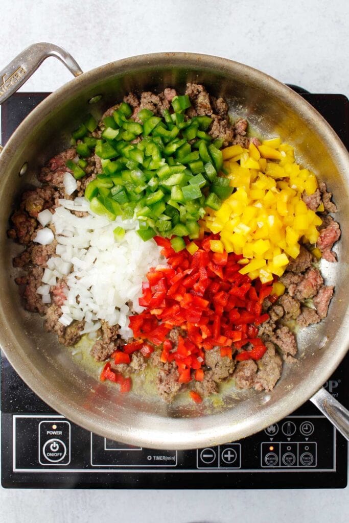 Cooking beef, ground bell peppers, and onions in a stainless steel pain.