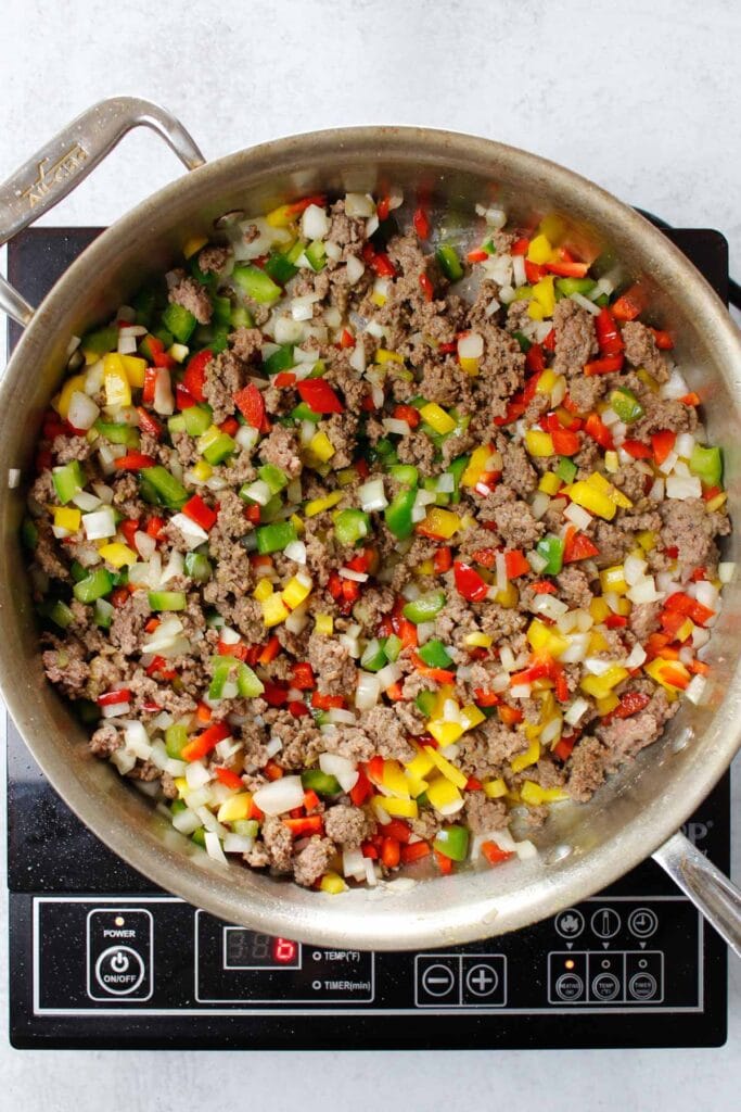 Cooking beef, ground bell peppers, and onions in a stainless steel pain.