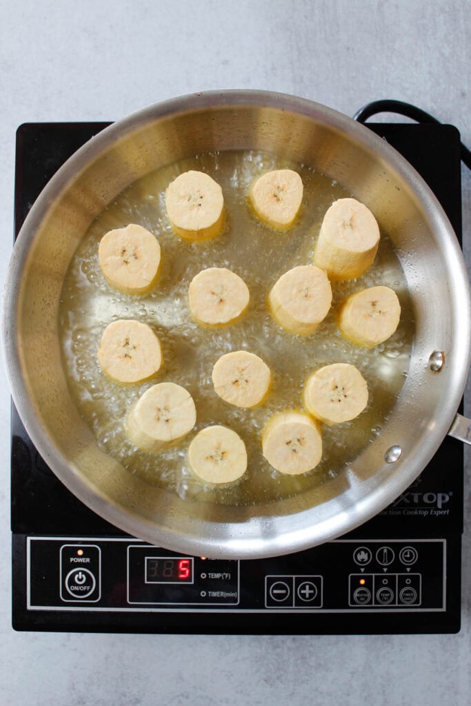 Frying tostones in a large skillet with vegetable oil.