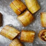 Golden brown green plantains frying in a large skillet with vegetable oil.