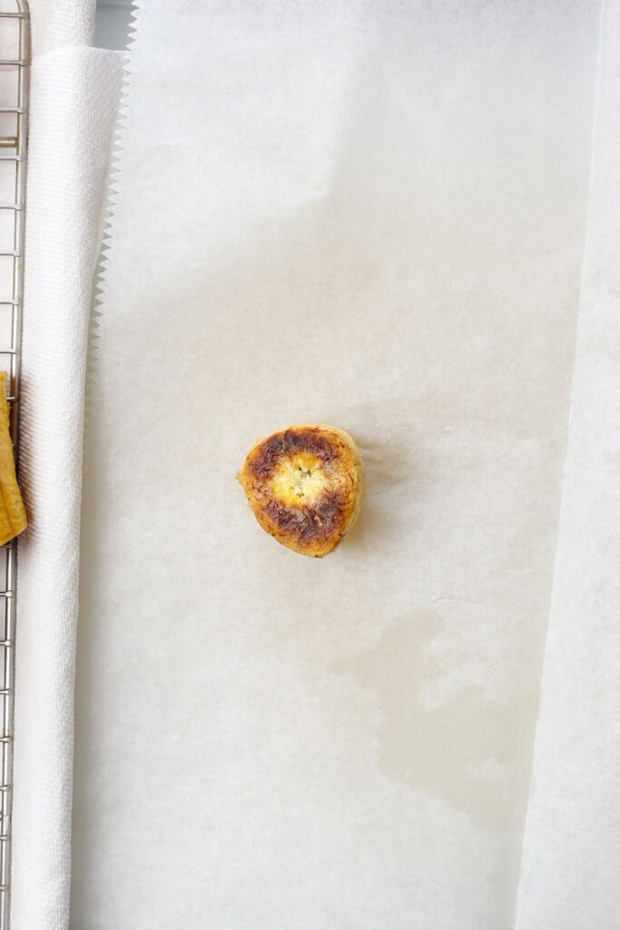 Single tostone on a sheet of parchment paper after the first fry.