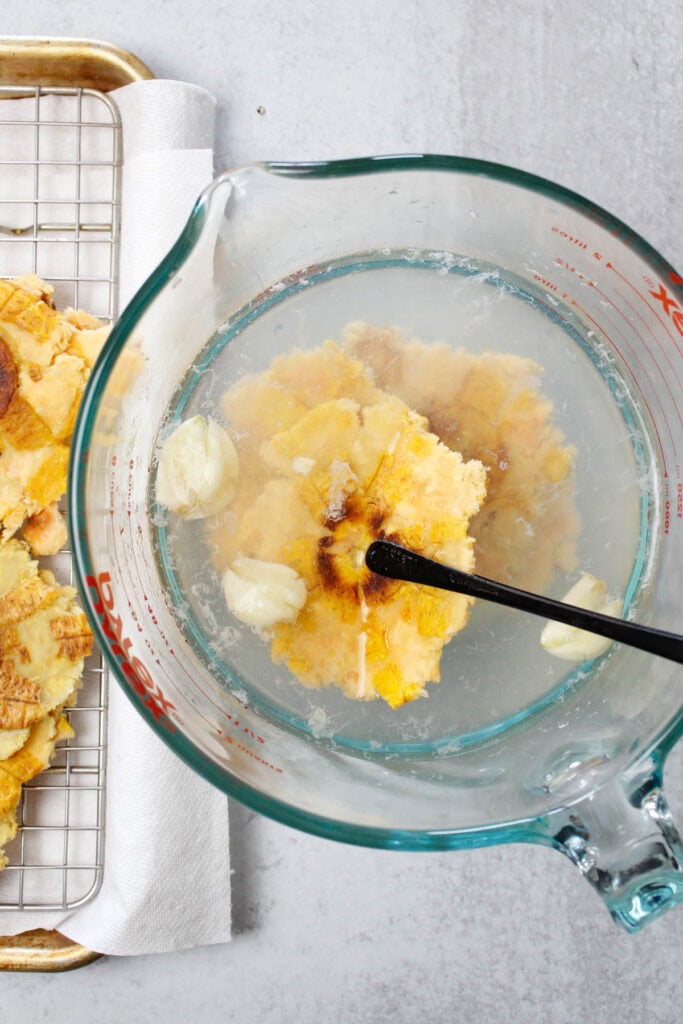 Flattened tostones being dipped into a garlic saltwater brine.