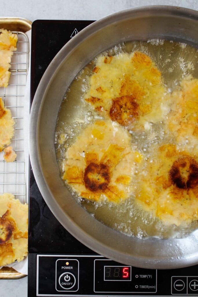 Frying pressed tostones for the second time in a large skillet.