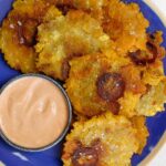 Tostones stacked on a blue plate with a small bowl of mayo-ketchup sauce.