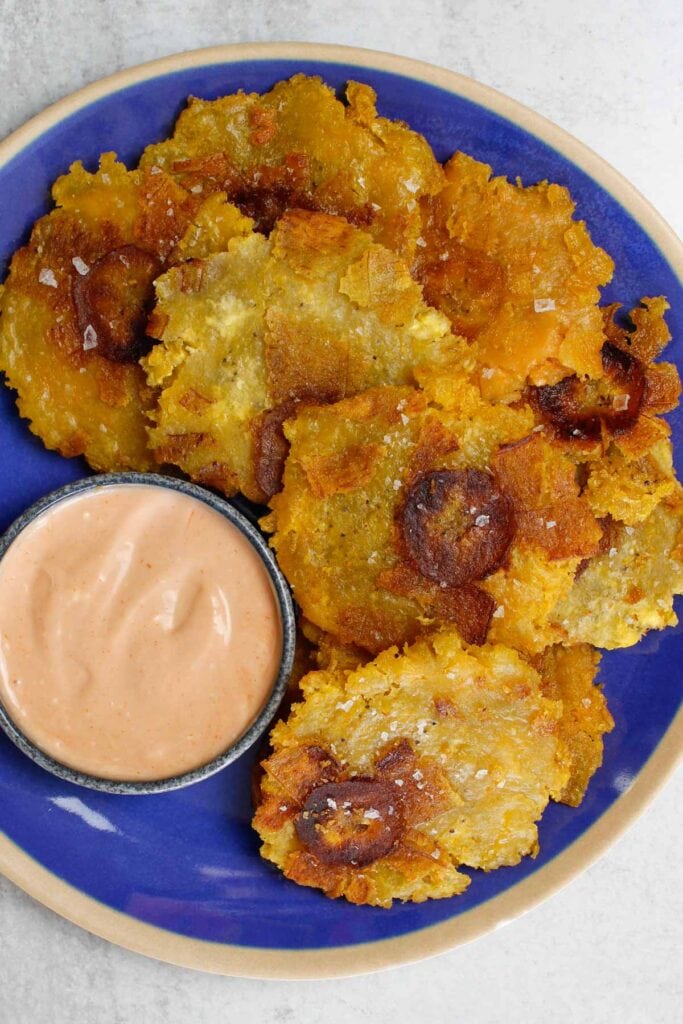 Tostones stacked on a blue plate with a small bowl of mayo-ketchup sauce.