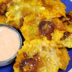 Tostones stacked on a blue plate with a small bowl of mayo-ketchup sauce.