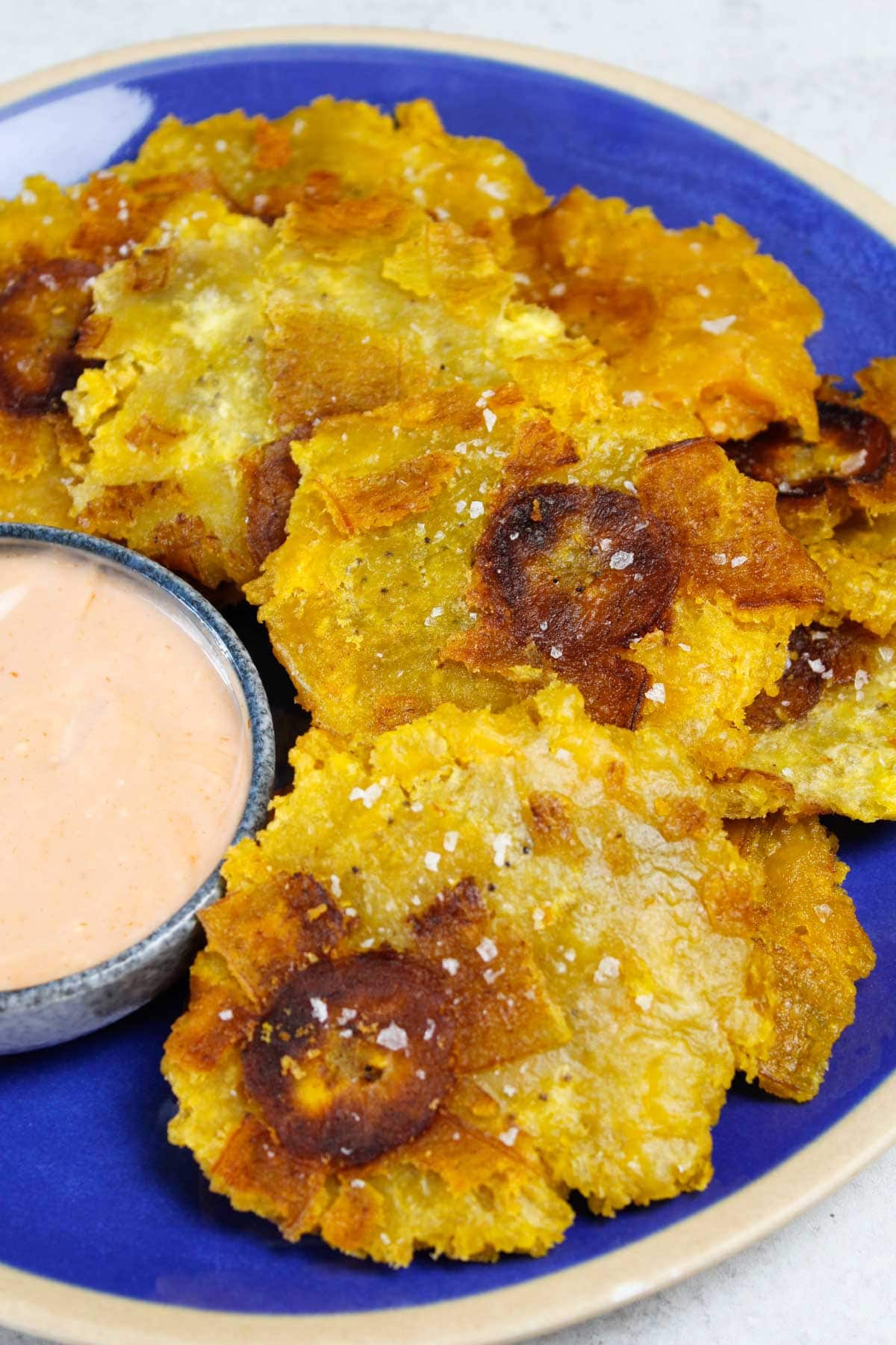 Tostones stacked on a blue plate with a small bowl of mayo-ketchup sauce.