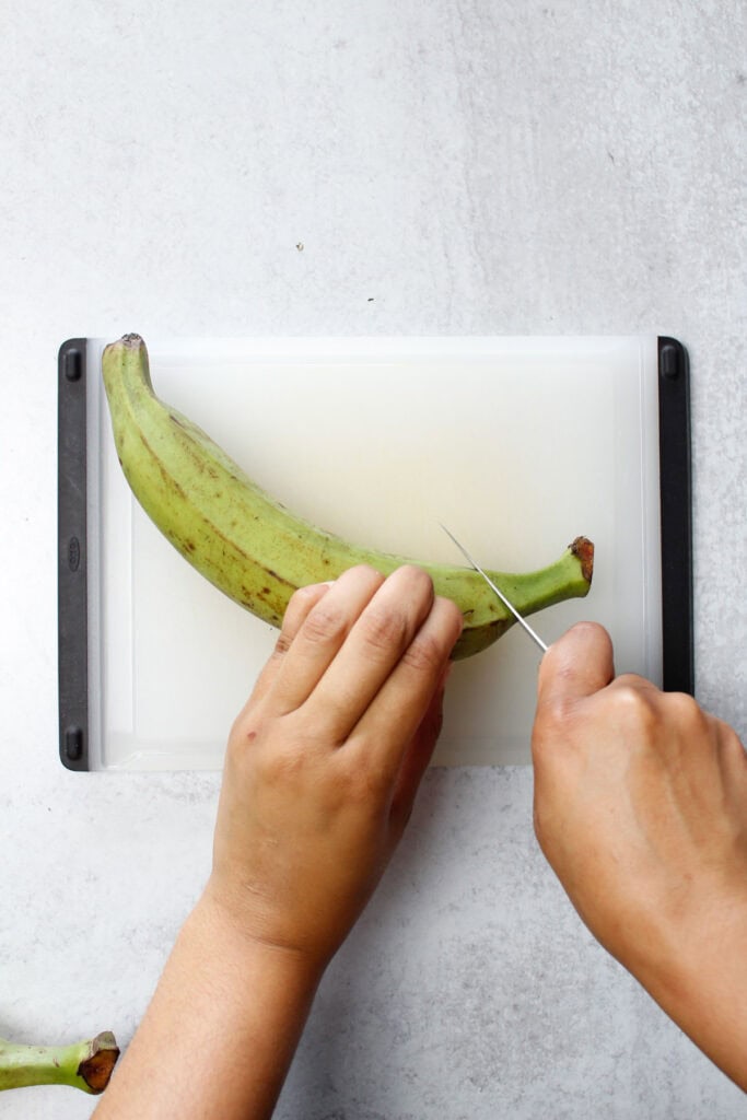 Cutting off the ends of a whole green plantain with a paring knife.