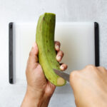 Slicing shallow cuts down the length of a green plantain using a paring knife.