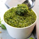 Pesto in a small white bowl being dug into with a silver spoon.