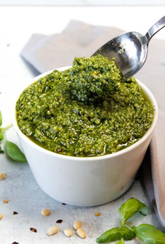 Pesto in a small white bowl being dug into with a silver spoon.