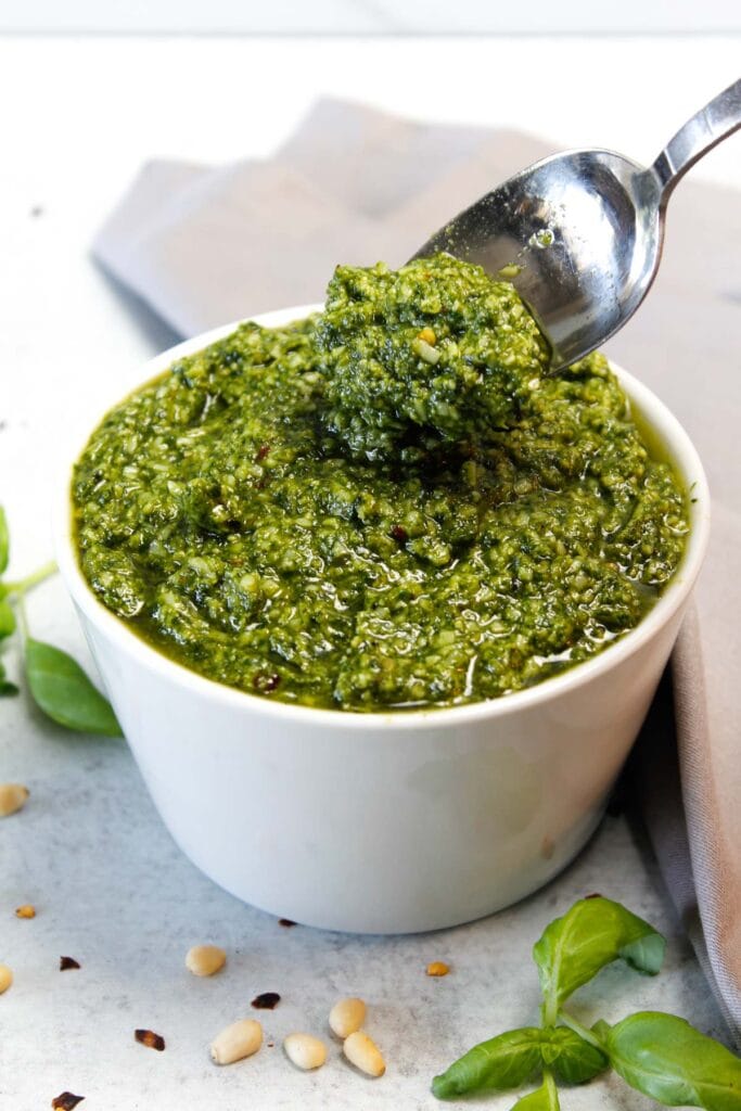 Pesto in a small white bowl being dug into with a silver spoon.