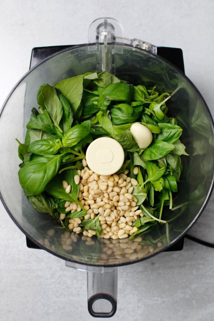 Pesto ingredients: basil, pine nuts, and garlic in a food processor.