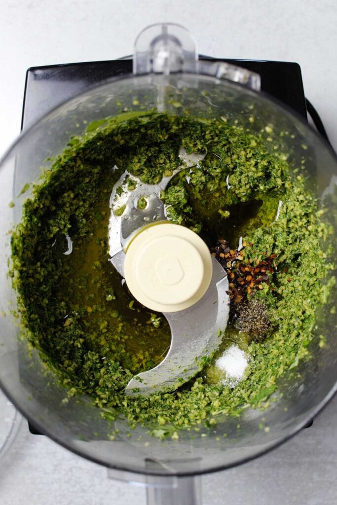 Pesto ingredients: basil, pine nuts, garlic, olive oil, and red pepper flakes in a food processor.