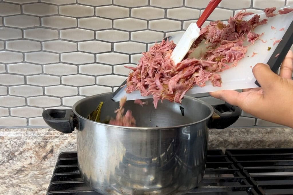 Adding shredded smoked turkey to pot of collard greens.