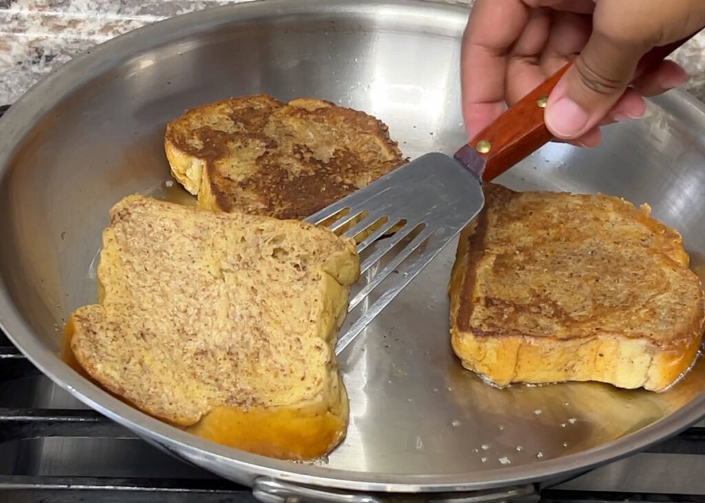 Flipping a piece of brioche french toast in a large skillet.