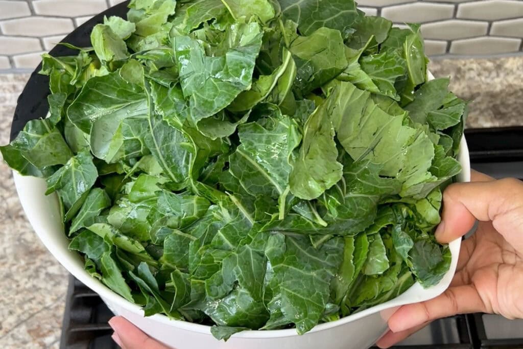 Cleaned and torn collard green leaves in a large white mixing bowl.