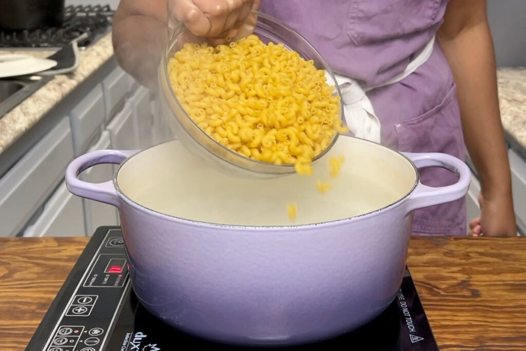 Boiling elbow noodles in a purple dutch oven.