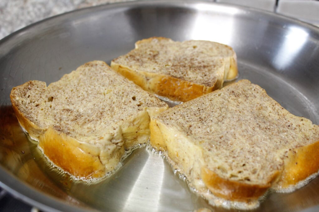 Closeup of Brioche french toast being cooked in a stainless-steel skillet.