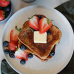 A stack of Brioche French Toast with strawberries, blueberries and a pat of butter.