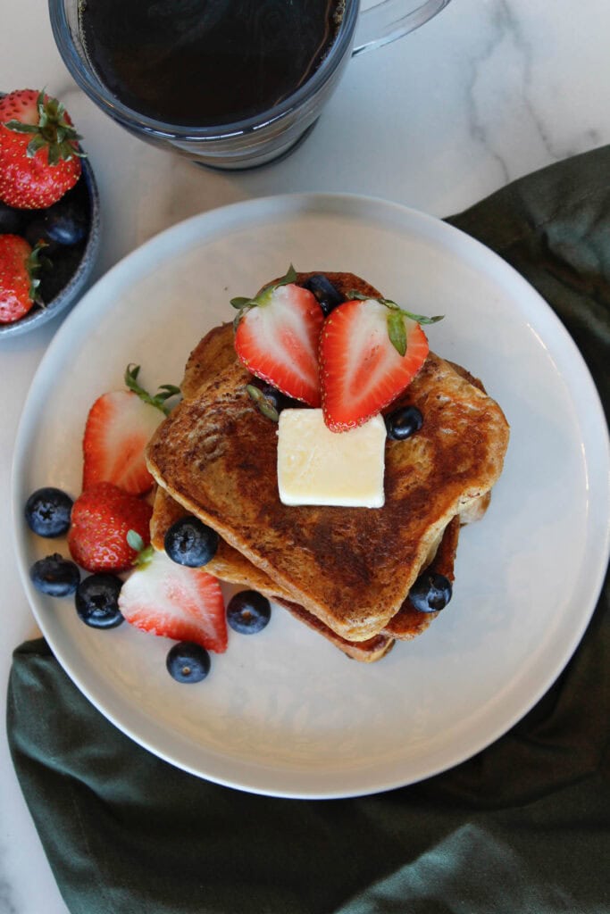 A stack of Brioche French Toast with strawberries, blueberries and a pat of butter.