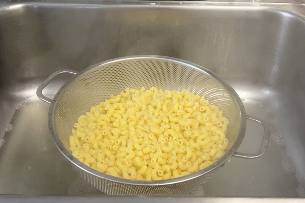 Draining cooked elbow noodles in a metal colander.