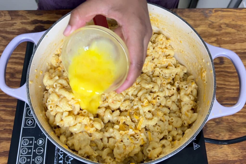 Pouring a beaten egg into elbow noodle and cheese mixture.