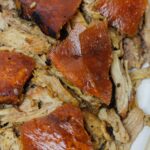 Shredded pernil on a platter, topped wth crispy pork skin.