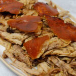 Shredded pernil on a platter, topped wth crispy pork skin.