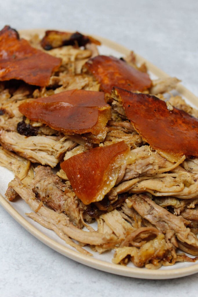 Shredded pernil on a platter, topped wth crispy pork skin.