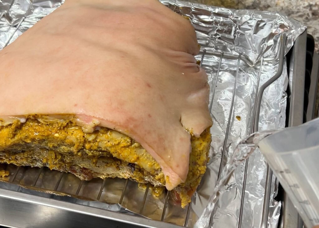 Pouring water into the bottom of a roasting pan with the pernil.