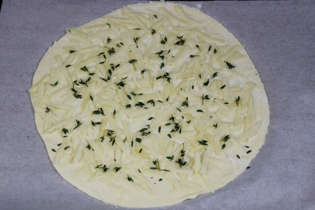 A puff pastry circle sprinkled with Gruyere cheese and thyme.