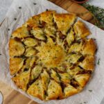 Caramelized French Onion Puff Pastry Twist on parchment paper surrounded by thyme and gruyere cheese.